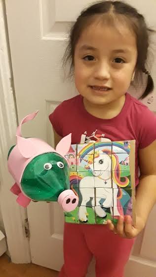 little girl holding up her unicorn puzzle and her recycled pig project